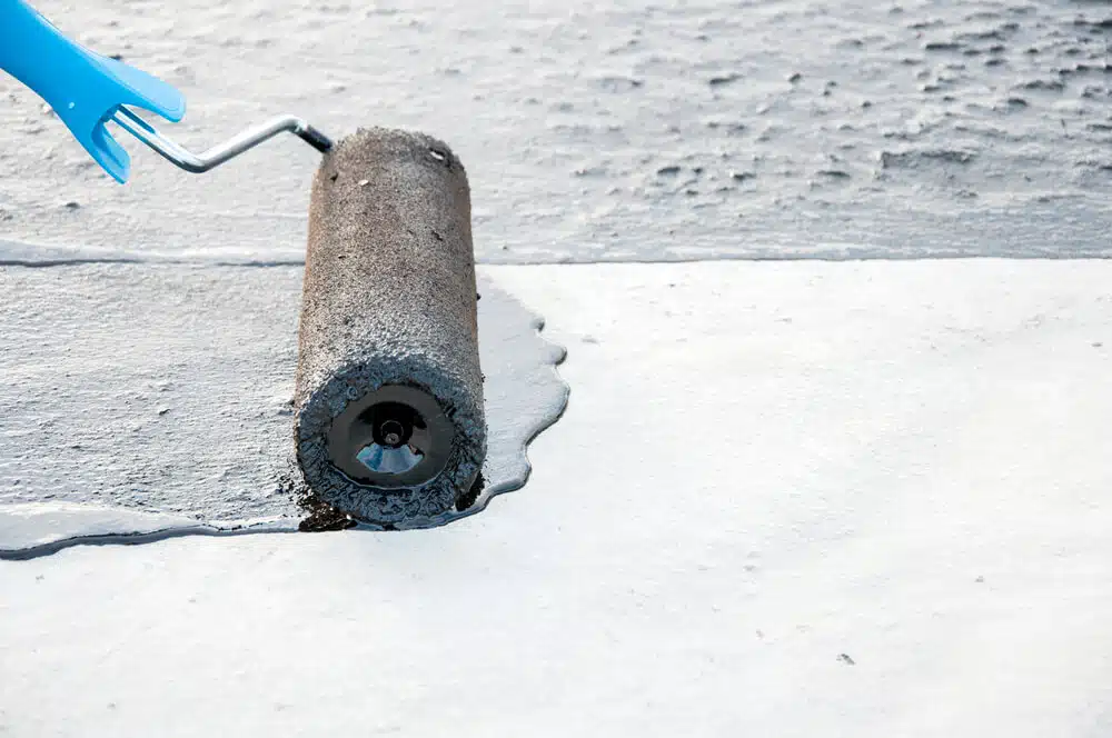 A roller spreading white protective coating across a flat roof surface