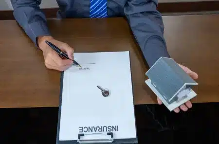 A person signing an insurance document while holding a small model house