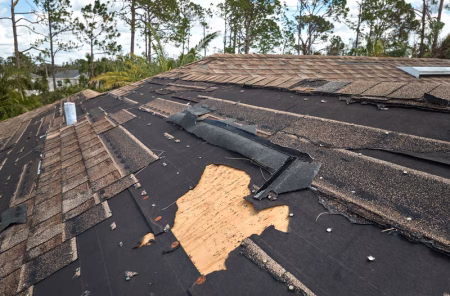 Damaged residential roof in New Orleans with missing shingles and exposed decking after a hurricane