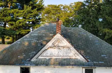 An aging asphalt shingle roof worn with moss on an older wood sided house