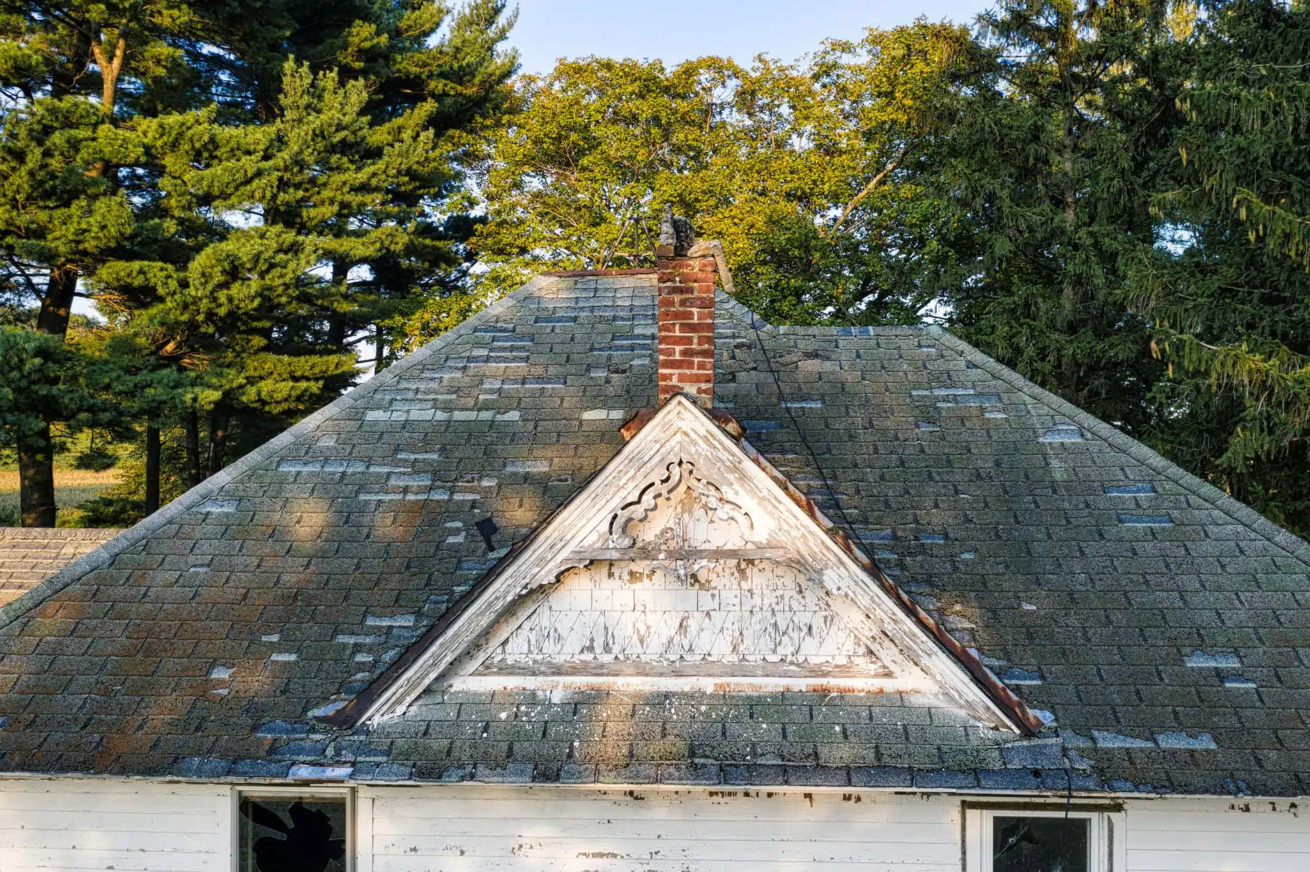 An aging asphalt shingle roof worn with moss on an older wood sided house